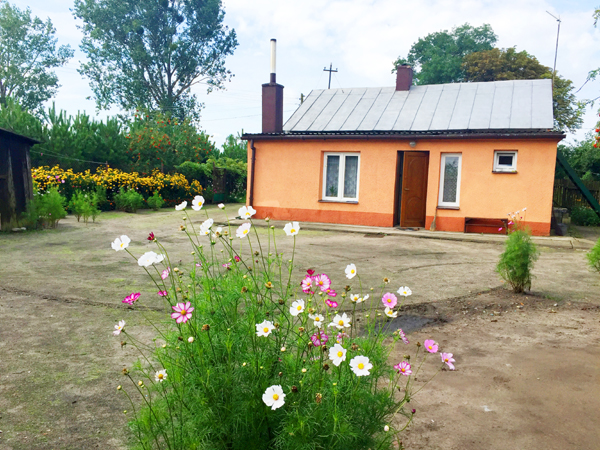 Fotografia domu wiejskiego z kwiatami na podwórku autorstwa Ani Wilanowskiej