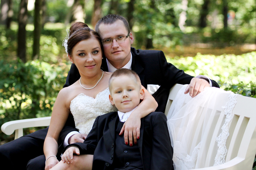 Fotografia młodej pary z dzieckiem na ławce wykonana w Łazienkach podczas sesji poślubnej autorstwa Ani Wilanowskiej.
