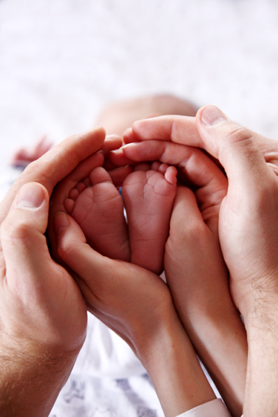 Fotografia dłoni rodziców obejmujących nóżki małego dziecka autorstwa Ani Wilanowskiej