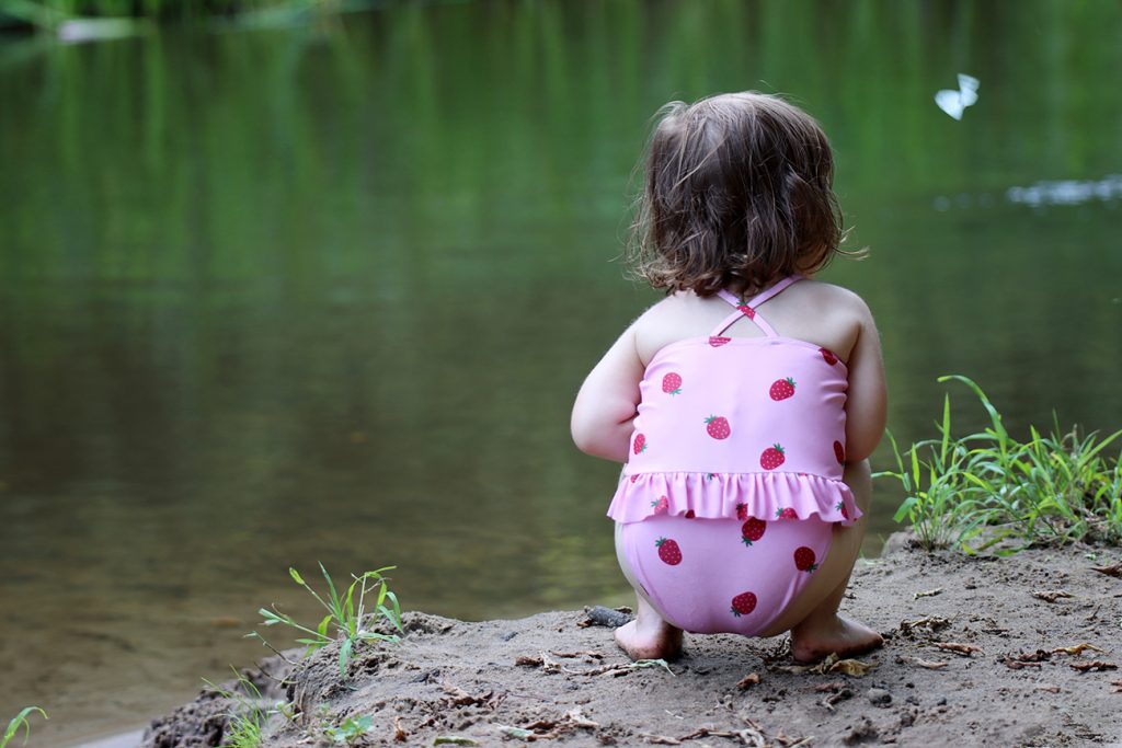 Zdjęcie dziewczynki latem nad wodą, oglądającej motyla, autorstwa Ani Wilanowskiej